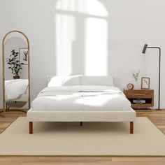 a white bed sitting on top of a wooden floor next to a mirror and lamp