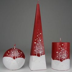 three red and white candle holders with trees painted on the sides, one has a christmas ornament next to it