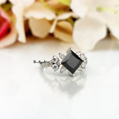 an engagement ring with black diamond surrounded by white diamonds on a table next to flowers