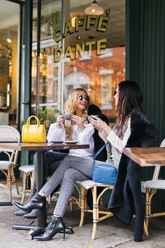 two women sitting at a table in front of a cafe