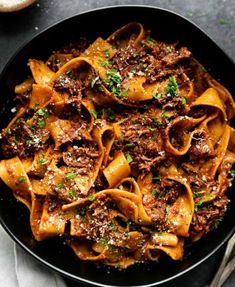 pasta with meat and parsley in a black skillet on a gray surface next to bread