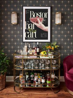 a bar cart with wine glasses and bottles on it in front of a wall mounted poster