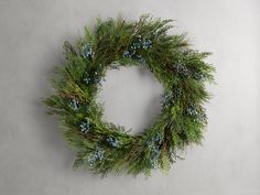 a green wreath with blue berries and pine needles hanging on a wall in front of a gray background