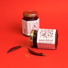 two jars of jam sitting on top of a red surface next to some dried chili peppers