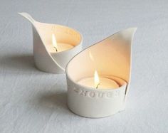 two white tea lights sitting on top of a white cloth covered table next to each other