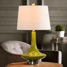 a green lamp sitting on top of a wooden table next to a gray chair with a white lampshade