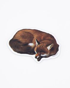 a brown and white fox sticker laying on top of a white surface with its eyes closed