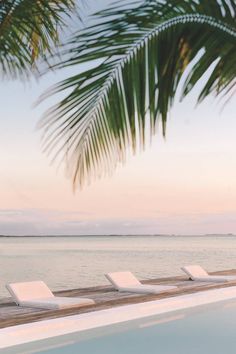 lounge chairs line the edge of an empty swimming pool near the ocean at sunset or sunrise