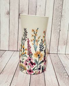 a vase with flowers painted on it sitting on a wooden floor next to a wall