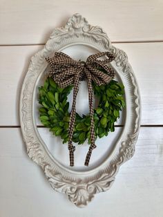 a white frame with a wreath and bow hanging on it