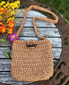 a crocheted purse sitting on top of a wooden table next to flowers and a vase