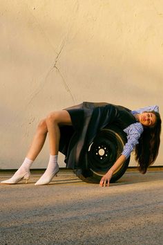 a woman laying on the ground next to a car tire with her legs spread out