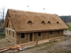 a house that is being built with straw on the roof and grass on the ground