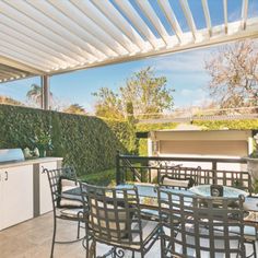 an outdoor kitchen and dining area with table, chairs, grill and bbq in the background