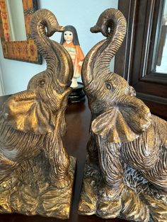 two statues of elephants on a table with a mirror in the backgrouf