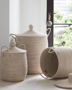 three woven baskets with handles and lids on the floor in front of a large window