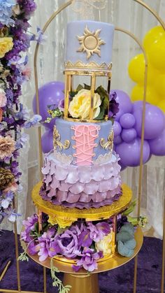 a three tiered cake sitting on top of a table next to purple and yellow balloons