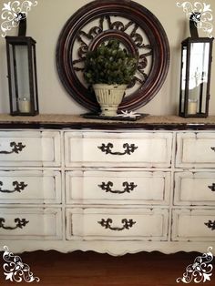 a white dresser with black drawers and two lanterns on top of it, in front of a mirror