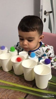 a little boy sitting at a table with cups