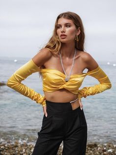 a woman standing on the beach with her hands on her hips wearing a yellow crop top