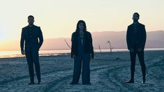 three men in suits standing on the beach at sunset