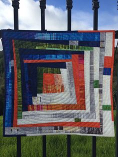 a quilt hanging on a fence in front of some green grass and blue sky with clouds