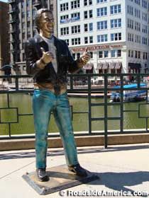 a statue of a man standing on top of a sidewalk next to a body of water