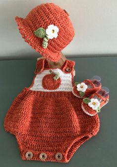 an orange crocheted baby outfit with matching hat and booties is displayed on a table