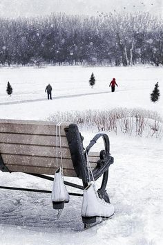 a park bench sitting in the middle of a snow covered field with people walking around