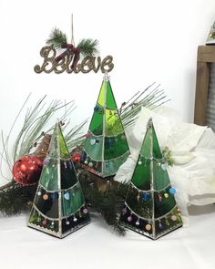 three green christmas trees with ornaments on them and the word believe spelled in gold lettering