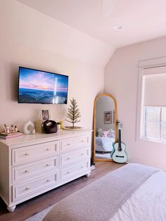 a flat screen tv sitting on top of a white dresser next to a bed in a bedroom