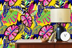 a colorful wallpaper with tropical leaves on it and a lamp next to the dresser