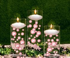 three glass vases filled with pink pearls on top of a table covered in greenery