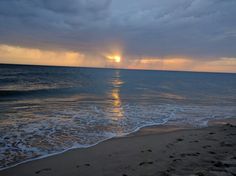 the sun is setting over the ocean with waves lapping in front of it,