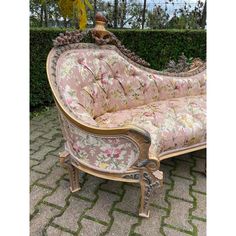 an ornately decorated couch sitting on top of a stone floor next to a hedge