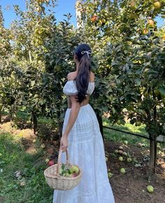 a woman in a white dress holding a basket full of apples