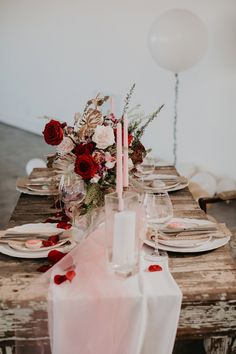 a wooden table topped with lots of plates and glasses next to a white balloon filled with red flowers