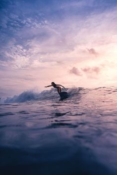 a person riding a surfboard on top of a wave in the ocean at sunset