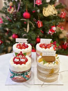 three cakes sitting on top of a white table next to a christmas tree with decorations