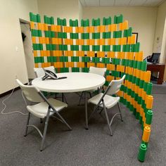 a room divider made out of green and yellow blocks with white chairs around it