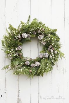 a wreath with pine cones and baby's breath is hung on a white wooden wall