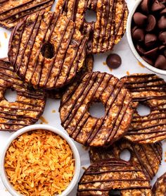 chocolate covered pretzels and other snacks on a white table with bowls of cereal