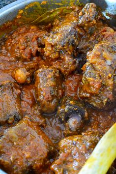 a pot filled with meat and sauce on top of a table next to a wooden spoon