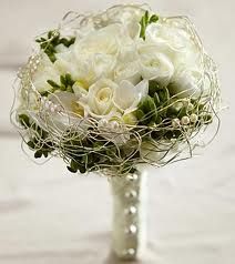 a bridal bouquet with white roses and greenery in a vase on a table