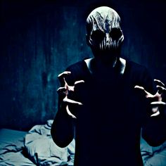 a man in a dark room with his hands out to the side while wearing a creepy mask