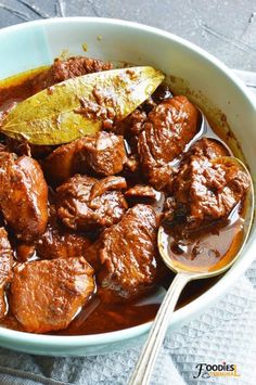 a bowl filled with meat and sauce on top of a table next to a spoon