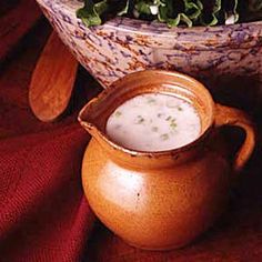 a pitcher filled with white liquid next to a bowl full of lettuce on a red cloth