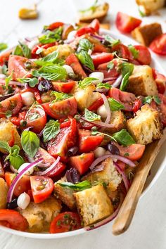 a salad with tomatoes, red onions and basil in a white bowl on a table