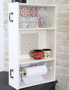 a white shelf with some cups on top of it and a roll of toilet paper in front of it