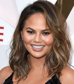 a close up of a person wearing a black dress and smiling at the camera with long wavy hair